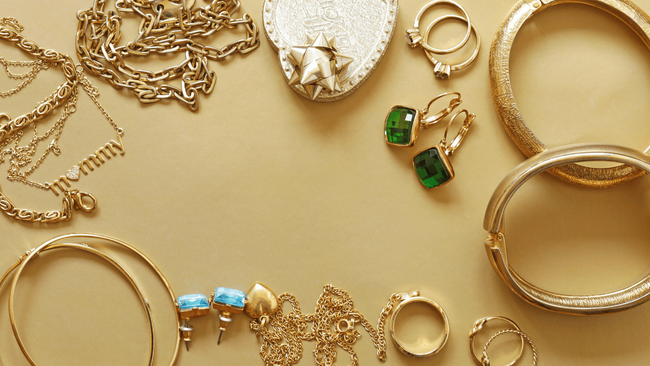 Gold chains and emerald earrings arranged on a warm tan surface.