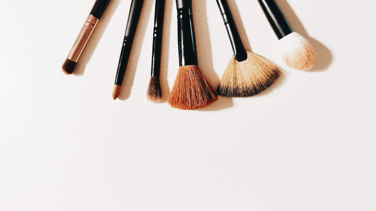 Six makeup brushes laid in a row on white, from dense to fan.